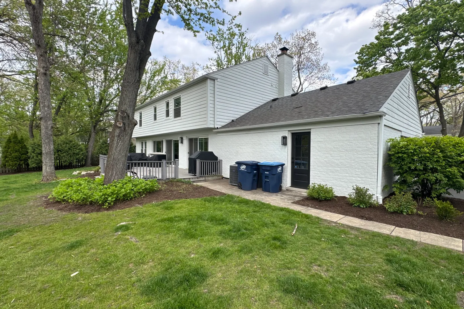 Rear elevation of a house from the lawn, with a dated deck, service walkway and condenser unit, photographed at site intake
