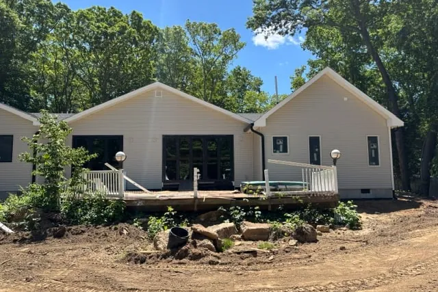 Site photograph of the rear elevation and deck with bare soil and a pile of cleared stone